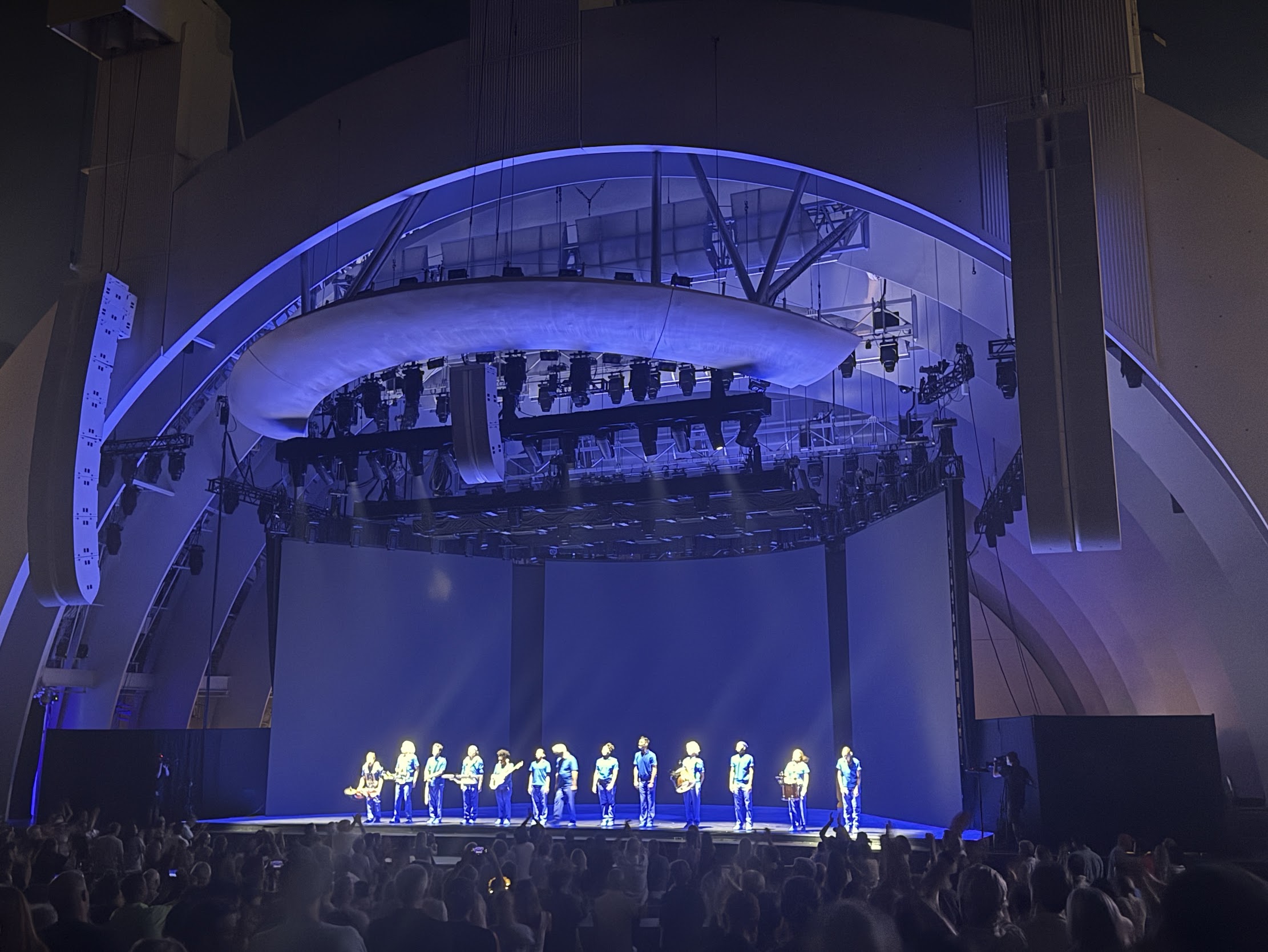 Performers on the Hollywood Bowl stage beneath blue lighting, with the audience in the foreground.